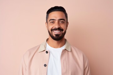 Obraz premium Portrait of handsome indian man looking at camera and smiling while standing against pink background