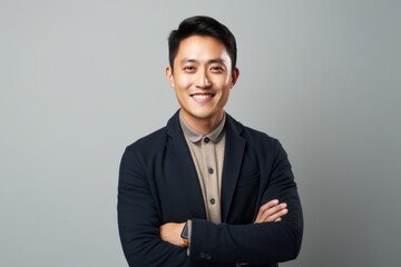 Portrait of a happy young asian business man standing over gray background