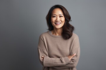 Fototapeta premium smiling asian woman in sweater with crossed arms isolated on grey