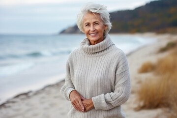 Fototapeta na wymiar senior woman with grey sweater on autumn beach, sea in background
