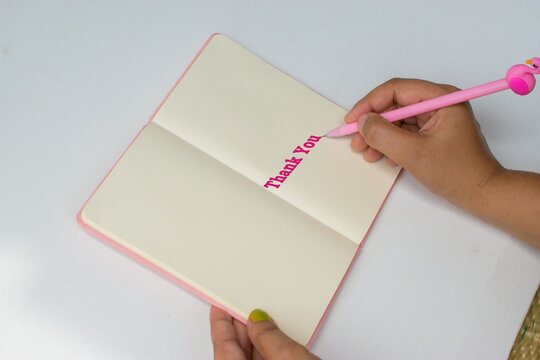 Right hand with pink pen writing  Thank you on notebook or diary. Copy space 