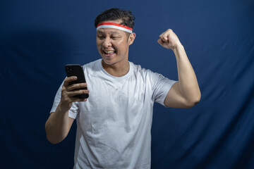 Cheerful young Asian man using mobile phone and celebrating Indonesia independence day on 17th...