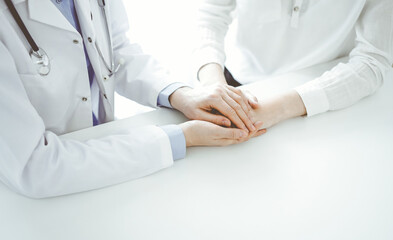 Doctor and patient sitting near each other at the table in clinic office. The focus is on female physician's hands reassuring woman, only hands, close up. Medicine concept