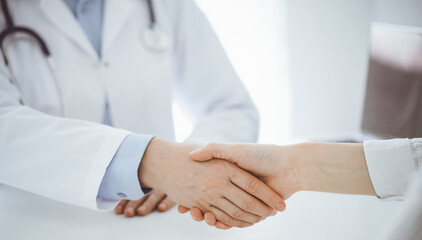 Obraz na płótnie Canvas Doctor and patient shaking hands while sitting opposite of each other at the table in clinic, just hands close up. Medicine concept