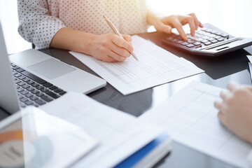 Woman accountant using a calculator and laptop computer while counting taxes for a client. Business...
