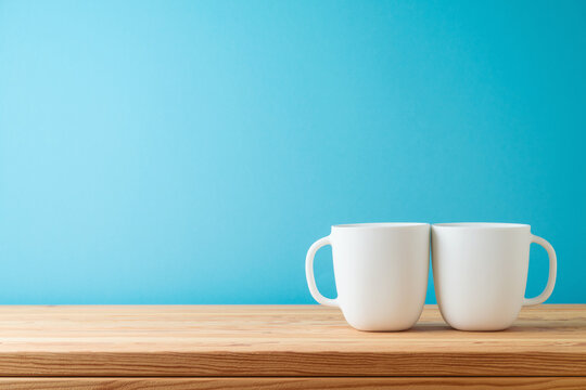 White coffee cups on wooden table over blue background. Kitchen mock up for design and product display