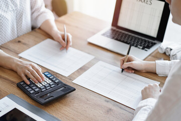 Two accountants using a laptop computer and calculator while counting taxes at wooden desk in office. Teamwork in business audit and finance