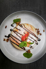 
Thick and fluffy American pancakes drenched in chocolate syrup with fresh strawberries and mint leaf