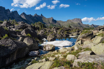 Amazing view of misty Lake Harmony with huge stones on the shore in Ergaki Nature Park. Summer landscape of crystal blue lake with rocks in mountain valley. Hiking in Western Sayan.