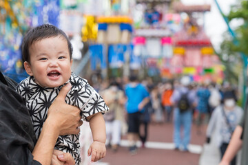 夏祭りで七夕飾りを見て笑顔になる甚平姿の生後9か月の赤ちゃんと抱っこする浴衣姿のパパ