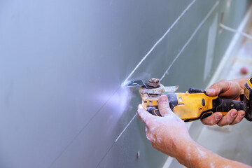 Cutting plasterboard with using multi tool for laying an electric cable in wall