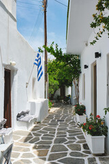 Picturesque narrow street with traditional whitewashed houses with greek flag of Naousa town in famous tourist attraction Paros island, Greece