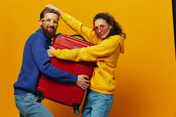 Obraz premium Woman and man smiling, suitcases in hand with yellow and red suitcase smiling merrily and crooked, yellow background, going on a trip, family vacation trip, newlyweds.
