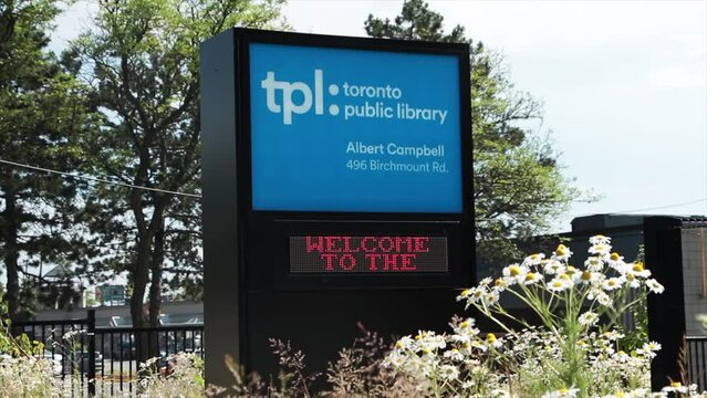 toronto public library albert campbell outdoor front entrance sign by path that also says in electronic writing welcome to the toronto public library, flowers in foreground