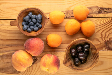 Fresh sweet fruits with wooden cups on wooden table, macro, top view.