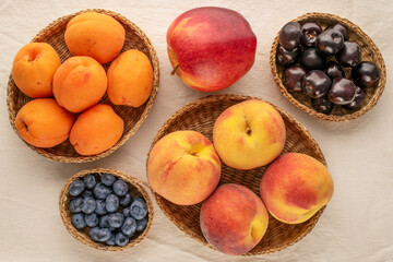 Fresh sweet fruits in straw plates on linen cloth, macro, top view.