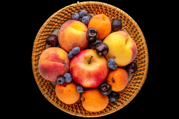 Fresh sweet fruits in a ceramic plate on a black background, macro, top view.