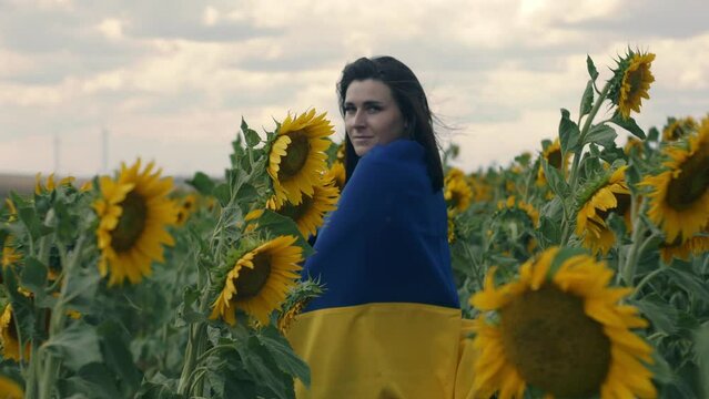 Portrait of a beautiful Ukrainian girl outdoor. Patriotic Ukrainian woman with blue yellow flag standing beetwen sunflowers in a field at windy weather