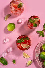 Strawberry mojito. Cocktail with rum, mint, lime and ice in a glass on a pink background. Homemade beverage.