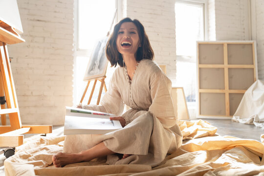 Young painter sitting on the ground reading in his studio
