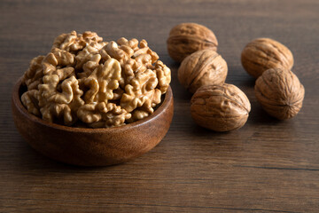 Peeled walnuts and whole walnuts in wooden bowl,top view
