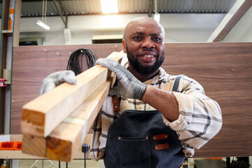 Portrait of middle-aged African craftsman carpenter wears apron, carrying wood planks, worker man makes wooden furniture in woodworking carpentry workshop, craftsman working at carpentry workshop.