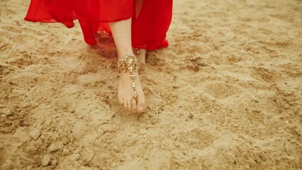 close-up female legs gold bracelets on feet walk on sand desert. woman in long red oriental silk abaya dress. Fantasy mystery girl fashion model posing stroll. Arabic nature yellow sands sunset Dubai