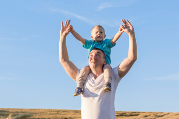 Dad and his little son are having fun walking in a field with ripe wheat. The child is sitting on the shoulders of the father. Grain for making bread. the concept of economic crisis and hunger.