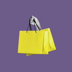 Antique female statue's hand holding yellow shopping paper bag isolated on violet color background....