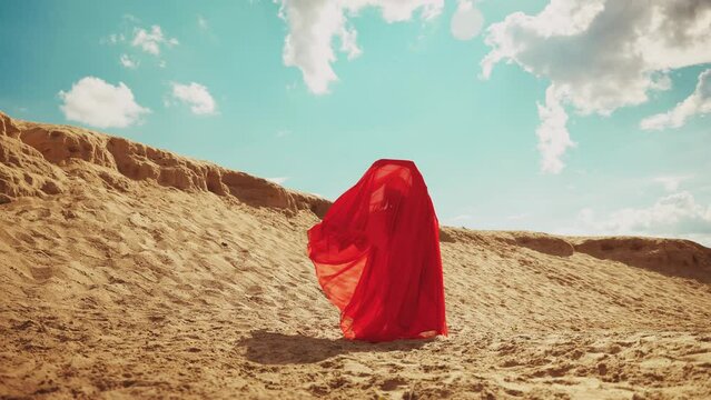 woman in red abaya dress dancing fly in wind hands raised to blue dramatic sky. Sexy girl arab style fashion model hides face under veil, silk fabric. Arabic nature sun yellow sand desert Dubai UAE 4k