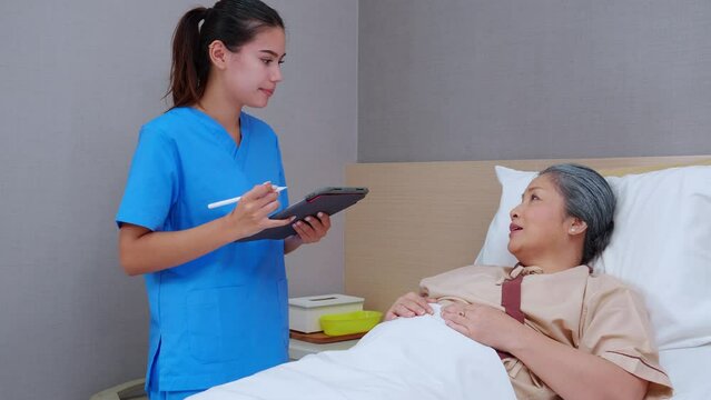 Nurse writing report document or prescription about medical and health care on digital tablet while explaining and check and diagnostic with elderly patient with sick in hospital, medical concept.