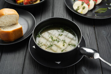 fresh soup broth on a plate on a black wooden background, set menu in a restaurant