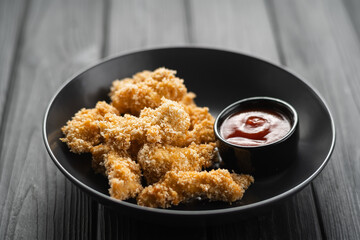 Delicious crispy chicken breast strips in breadcrumbs with tomato sauce on a plate on a black wooden background