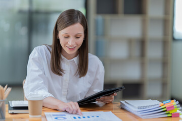 Sharing good business news. Attractive young businesswoman talking on the mobile phone and smiling while sitting at her working place in office and Checking document.