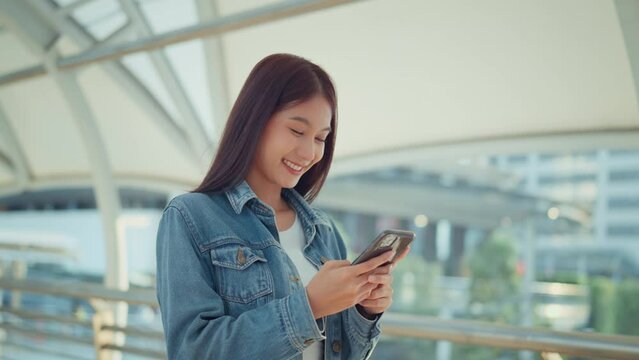 Happy young asian woman using mobile phone with chatting online with friends, Female in jean jacket sitting in the city using social media on smartphone, Technology