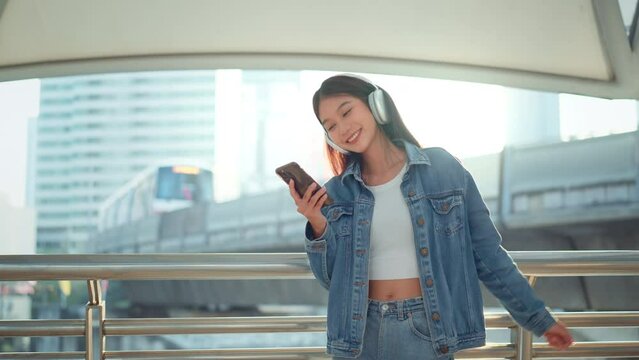 Happy young asian woman wearing headphones and enjoying music on the urban street city, Smiling female listening to music and dancing alone.