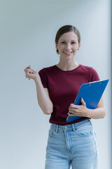 Young and attractive woman smiling at the camera, looking professional and ready to do business with a white background. Wearing a T shirt, holding document.
