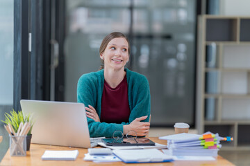Obraz premium Sharing good business news. Attractive young businesswoman talking on the mobile phone and smiling while sitting at her working place in office and looking at laptop PC