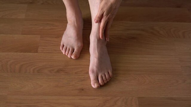 Hallux valgus on female legs on the background of laminate flooring. A bump on a woman's legs close-up. View from above.