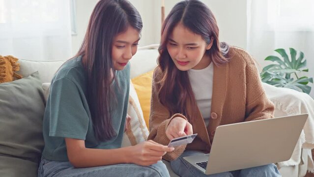 Excited happy two roommates shopping online together with mockup credit card and laptop sitting on a sofa at home, Online payment, easy and digital payment for ecommerce