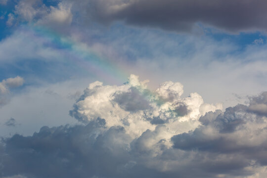 A gorgeous rainbow in the clouds, reminiscent of heaven or the rainbow bridge. Beautiful puffy white and gray clouds with a touch of blue sky and a stunning little rainbow. Sonoran Desert sky. 