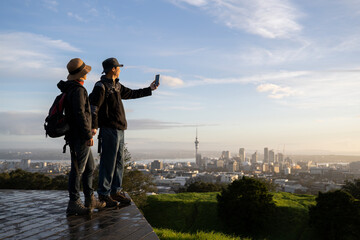 Couple taking photo with smartphone on Mt Eden summit at sunrise. Skytower in the background....