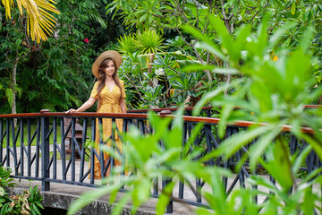Young woman on bridge in tropical resort, smiling in beautiful garden with palm trees. Concept of summer vacation and tropical lifestyle.