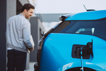 Man with laptop leaving electric car charging