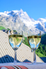 Drinking of dry white Roussette de Savoie and Vin de Savoie wine from Savoy region with view on Hautes Alpes mountains with snow on tops in summer