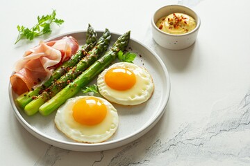Breakfast fried eggs with fresh asparagus and ham (jamon), herbs in a plate on a white background. Delicious hearty brunch.