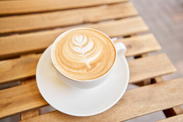 Cup of hot cappuccino. The table in the coworking space of the coffee shop. A cup of coffee on the veranda on a sunny day. Coffee break at the cafe. Close-up