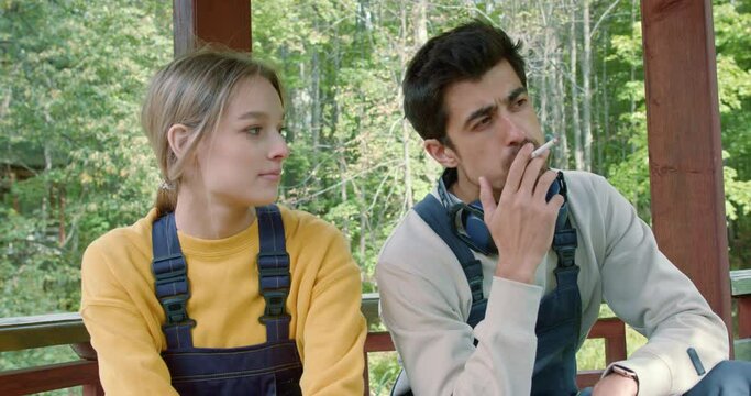 male and female workers having pause, rest after work. They sit on bench , smoke a cigarette. Taking a break from work, recuperating. Stopping work. Rest of employees. man gives cigarette to woman