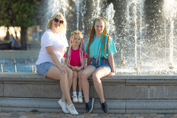 Mother with two happy girls sisters in a bright summer t-shirt with colored African braids in the...