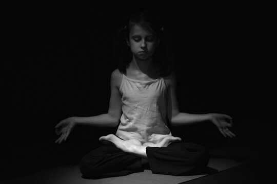 Young yogi girl practicing yoga lesson, breathing, meditation, doing Ardha Padmasana exercise, Half Lotus pose with mudra gesture, working out. Black and white image.